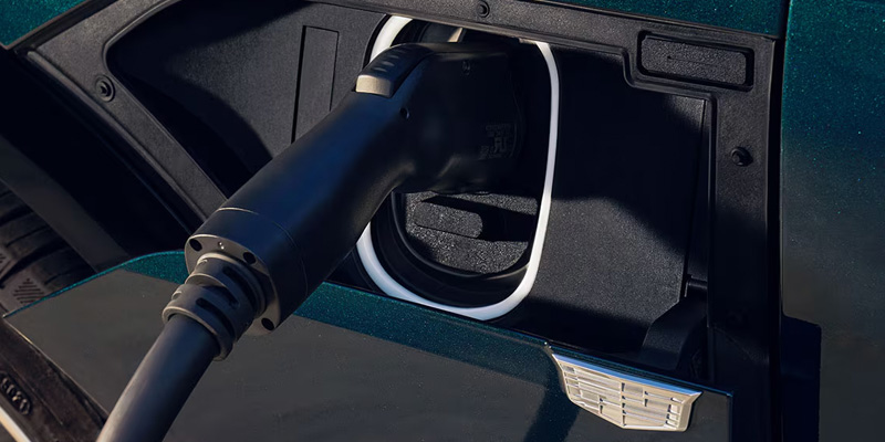 A close-up of an electric vehicle charging cable plugged into the side port of a dark green Cadillac LYRIQ.