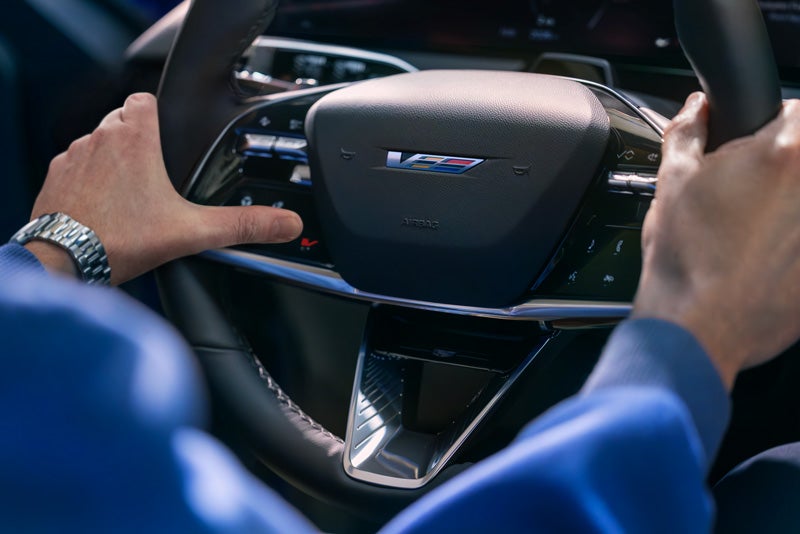 Close-up of a Man About to Press the V-Button on the 2026 OPTIQ-V Steering Wheel | Airport Cadillac in Medford OR