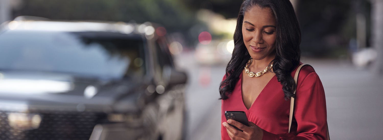 lady checking her mobile with a Cadillac vehicle background | Airport Cadillac in Medford OR